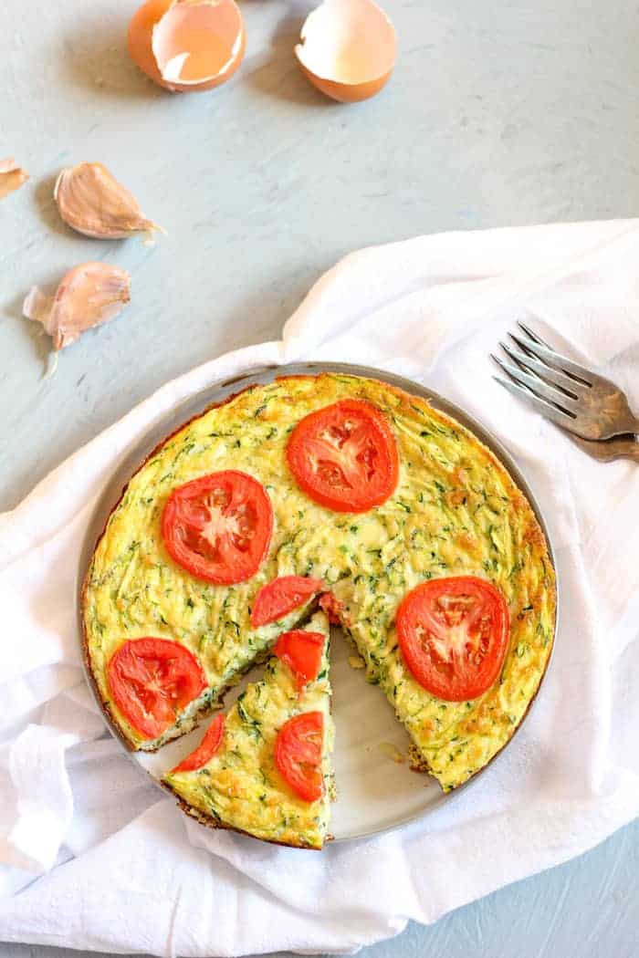 Image, taken from above, shows a dish of zucchini frittata on a white napkin next to a fork