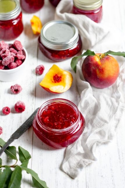 Image shows several jars of jam, with peaches and raspberries nearby