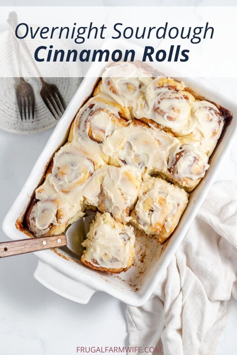 Image, taken from above, shows a white pan of sourdough cinnamon rolls with a spatula taking on roll from the pan.
